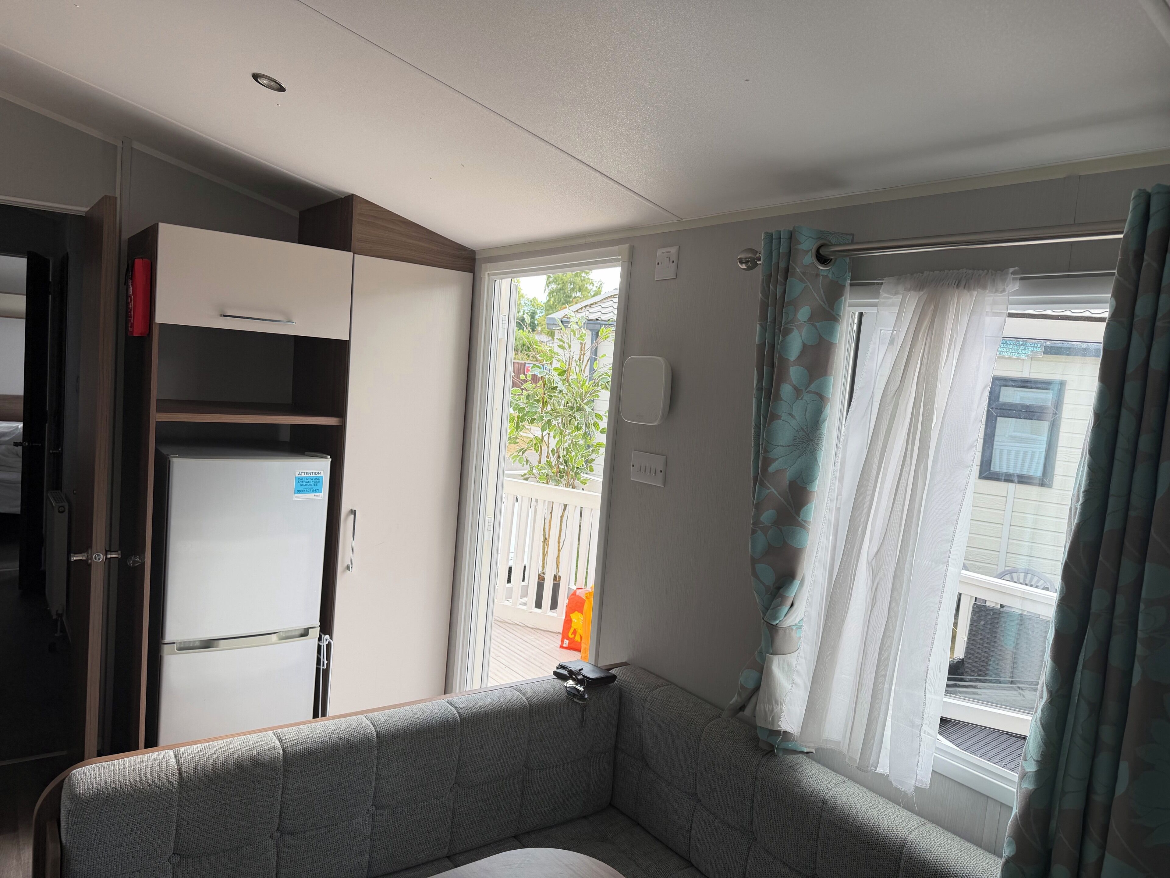 Quarto com sofá, um armário branco com um adesivo azul e uma janela com cortinas.