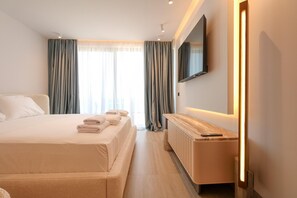 A hotel room with a bed, a bedside table, a TV mounted on the wall, and a window with curtains.