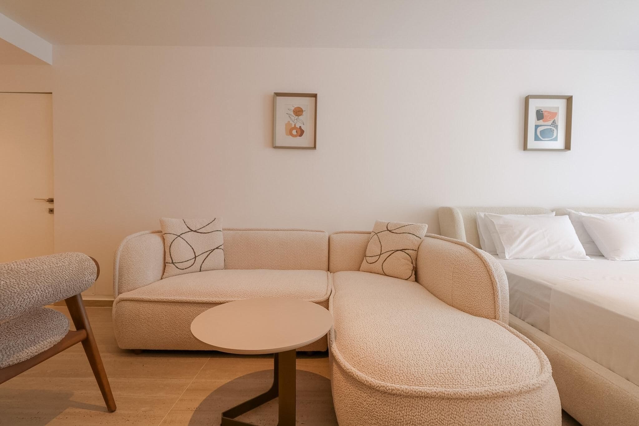 A modern, minimalist living room with a sofa, a round coffee table, and two framed artworks on the wall.
