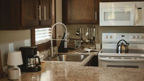 Una cucina con un lavello in acciaio inox, un bollitore sul fornello e vari utensili appesi al muro.