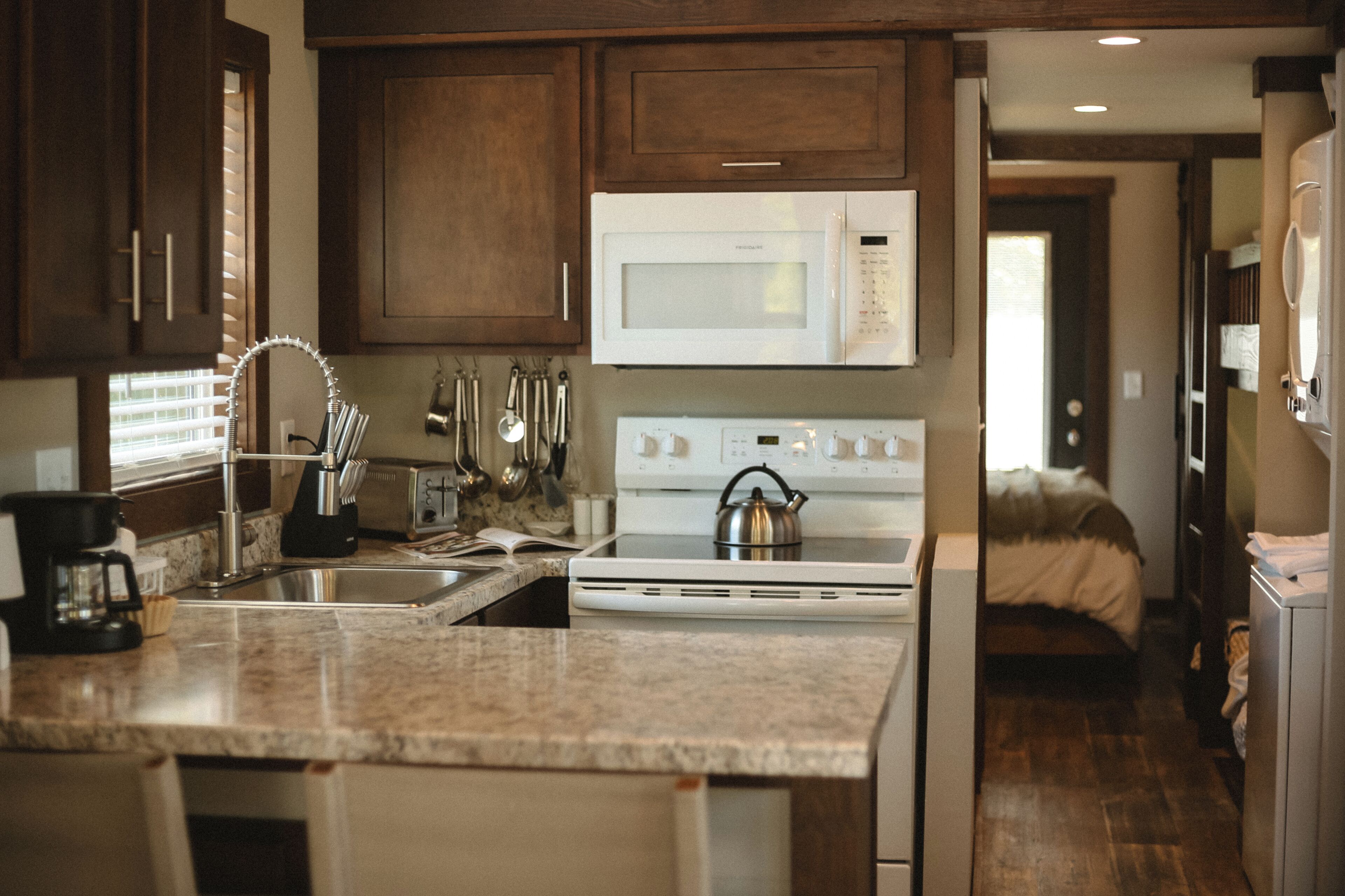 A kitchen with a microwave, stove, sink, and various utensils.