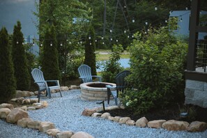 Un espace patio aménagé avec deux fauteuils Adirondack, un foyer en pierre et des guirlandes lumineuses.