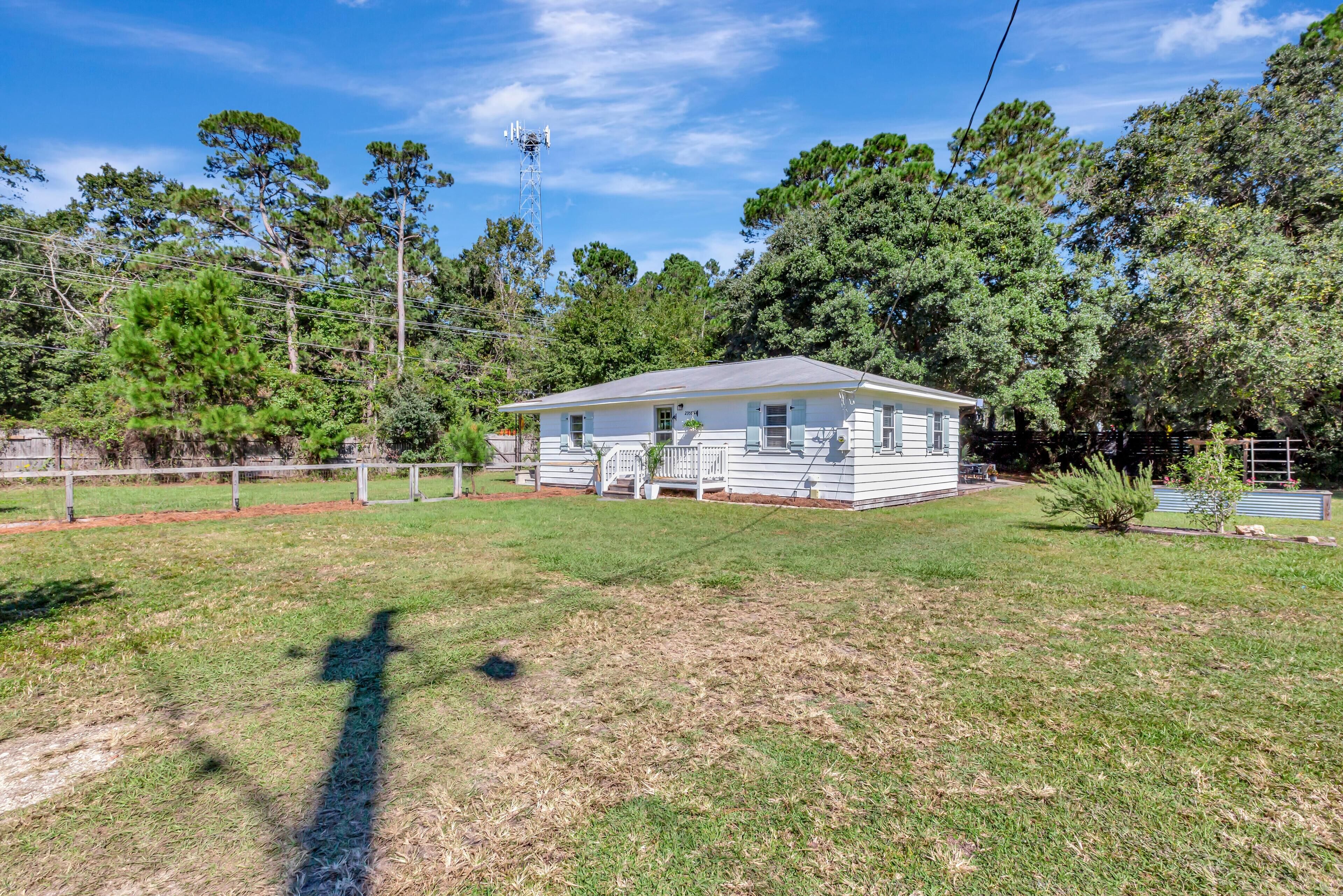 A single-story house with a front porch, surrounded by a fenced yard and trees.