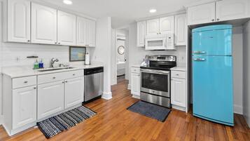 Una cocina con muebles blancos, un refrigerador azul, electrodomésticos de acero inoxidable y pisos de madera.