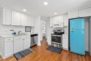 Una cocina con muebles blancos, un refrigerador azul, electrodomésticos de acero inoxidable y pisos de madera.