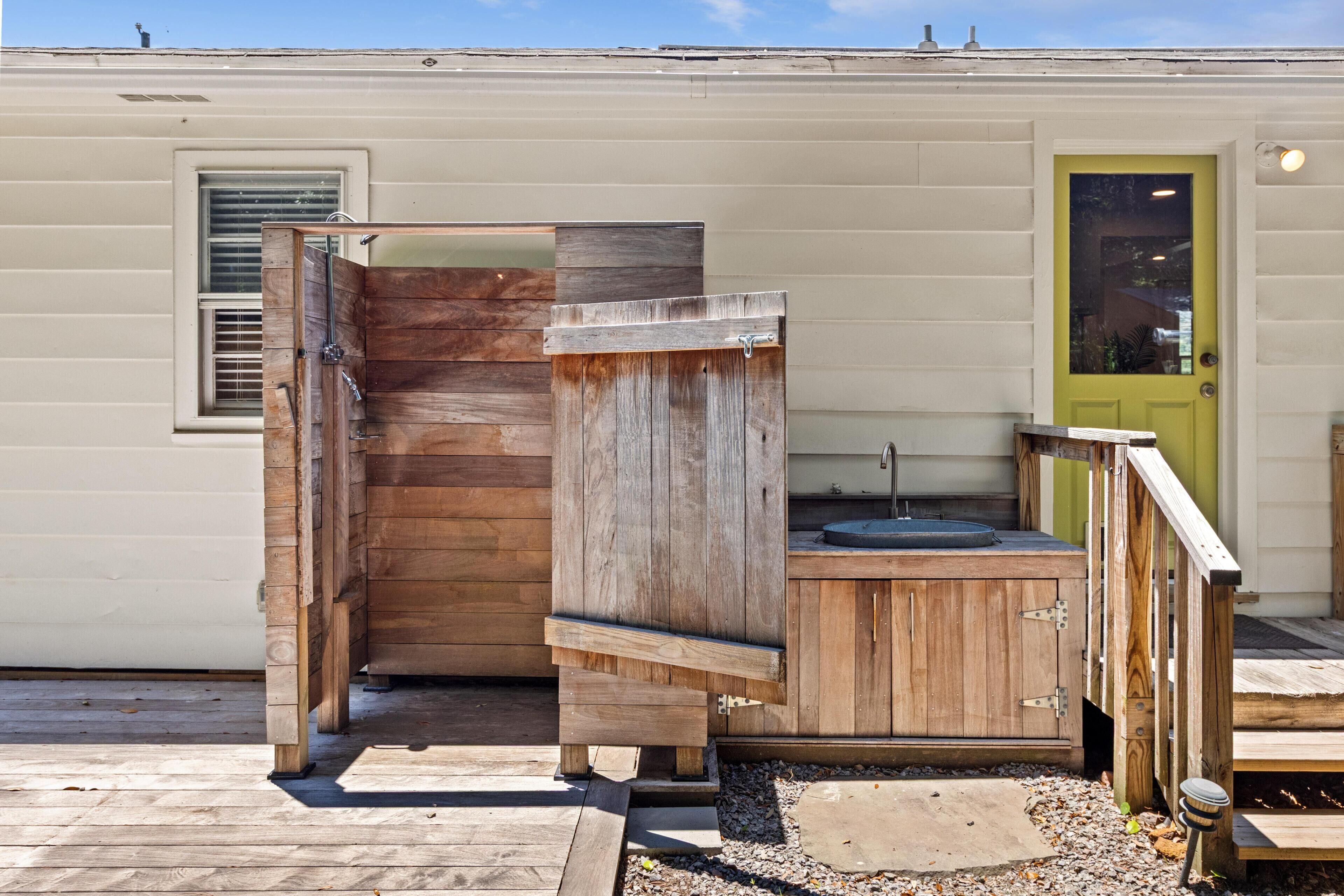 Un área de ducha exterior de madera con puerta, lavamanos y una pequeña terraza.