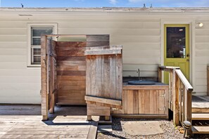 Un área de ducha exterior de madera con puerta, lavamanos y una pequeña terraza.