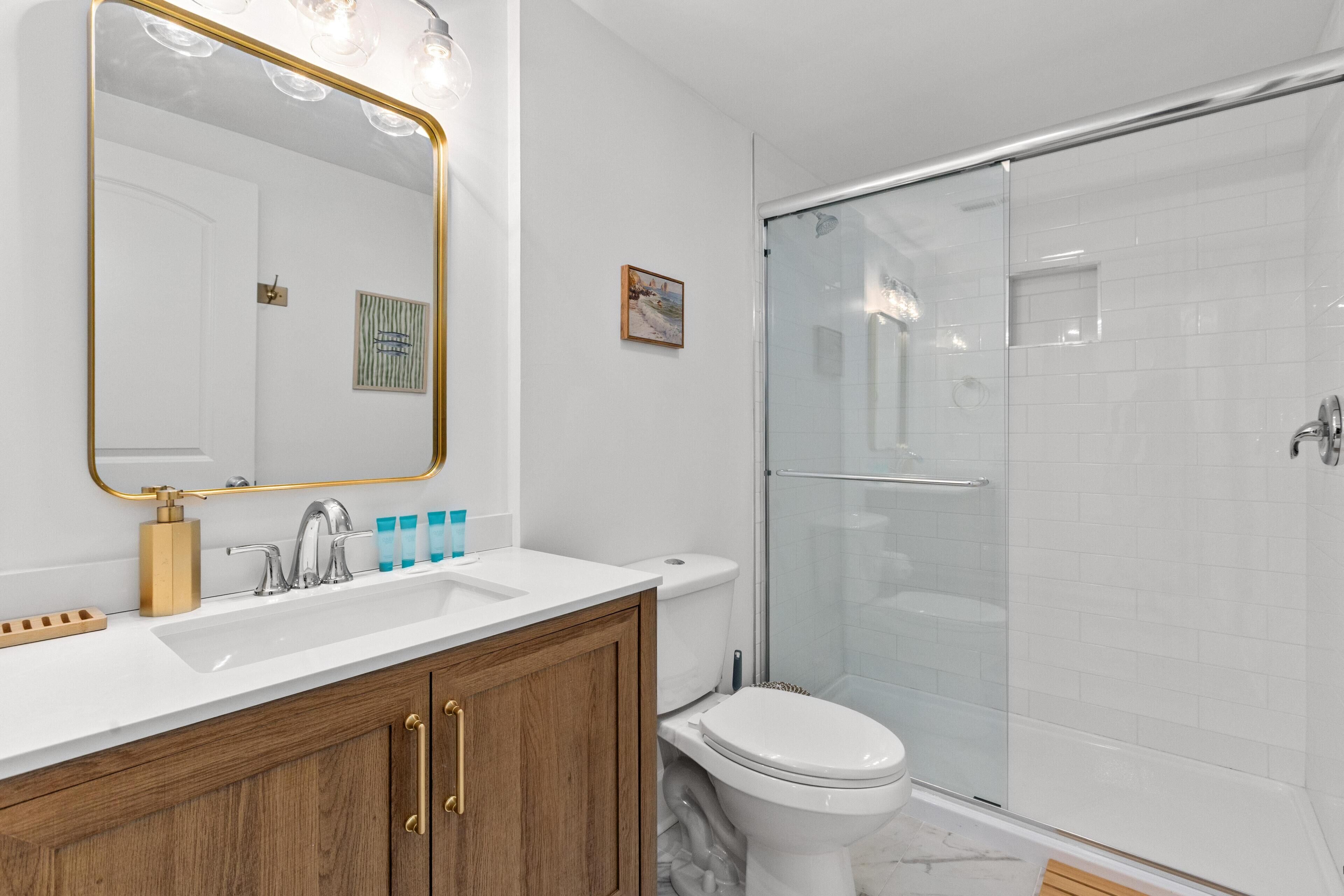 Un baño con lavamanos blanco, un espejo con iluminación, inodoro y cabina de ducha de vidrio.
