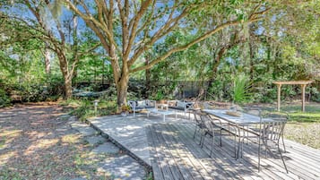 A deck with outdoor furniture, surrounded by trees and a garden.