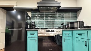A kitchen with a black refrigerator, a stove, and teal cabinets. - Modern Craftsman Home in Houston's Historic 1st Ward/Heights (Houston)