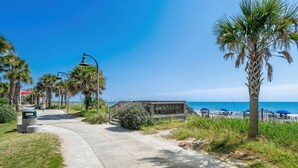 A coastal walkway with palm trees, a wooden fence, and beach umbrellas. - Pier View-sleeps 10-pets-walk to Beach (Myrtle Beach)
