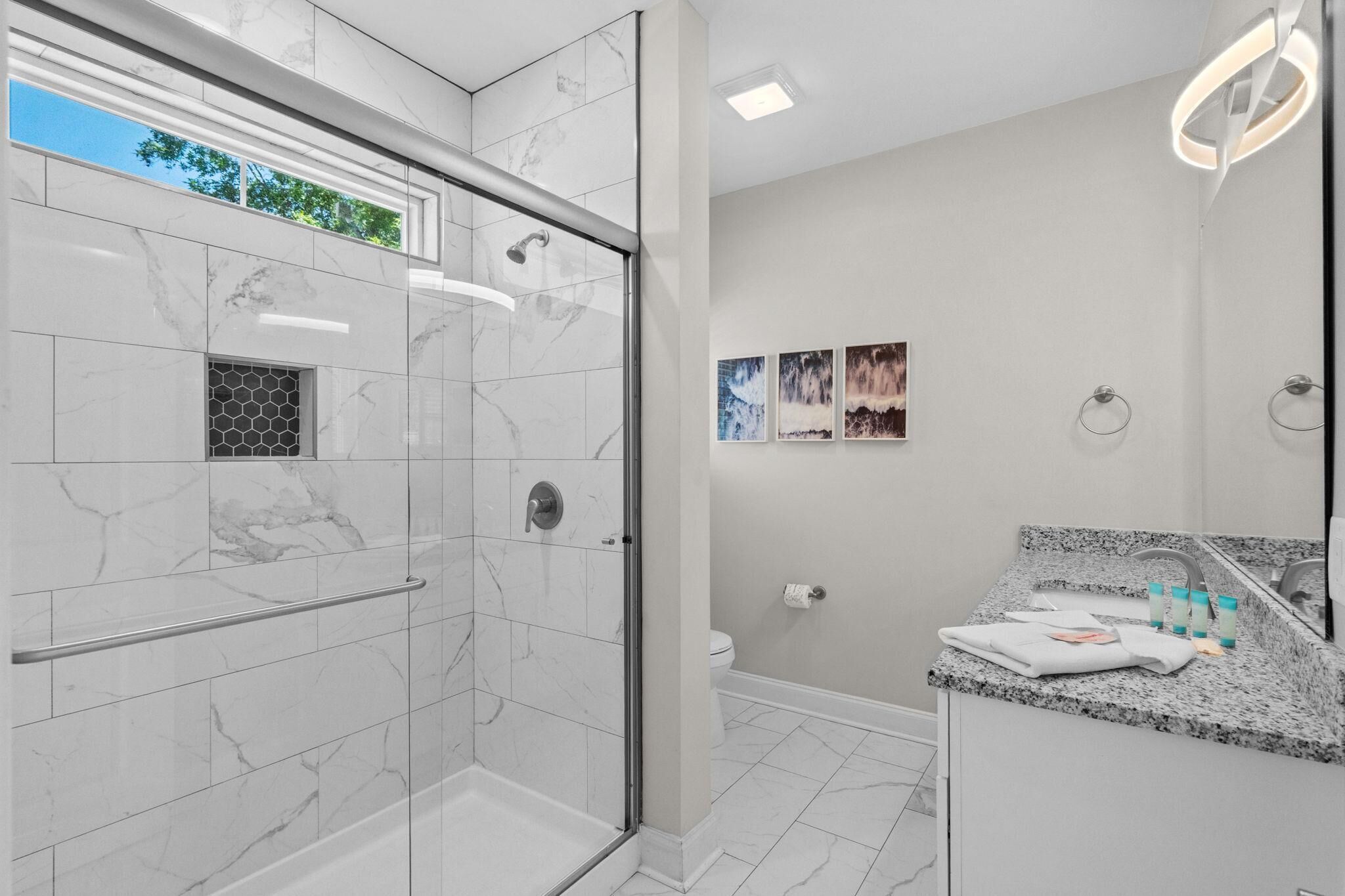 A modern bathroom with a glass shower enclosure, a marble-tiled floor, a granite countertop, and a wall-mounted sink with a mirror.
