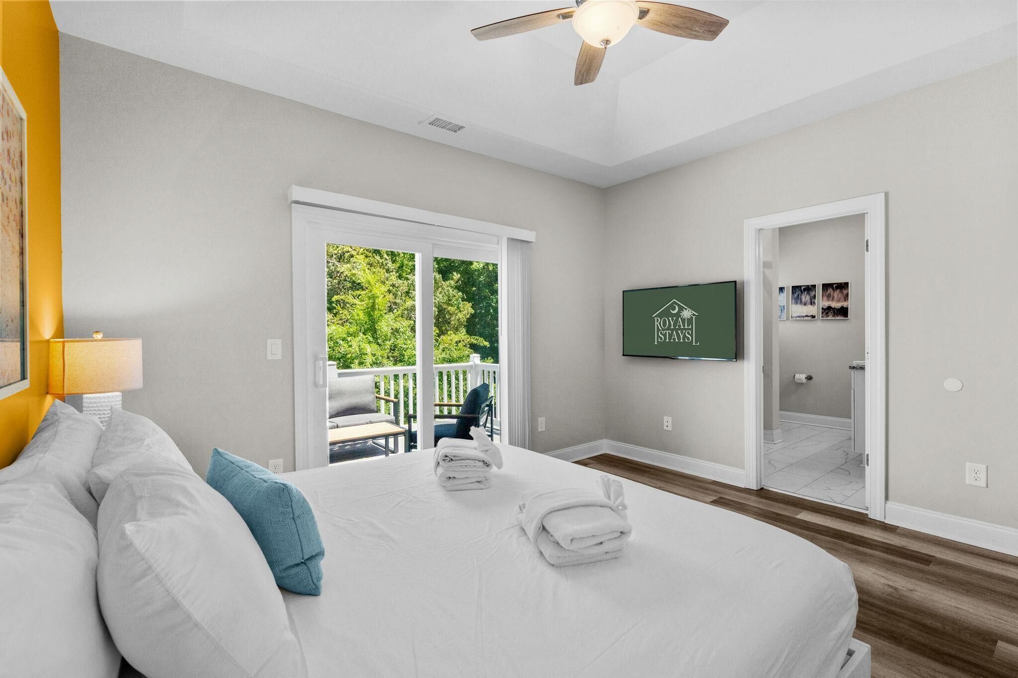 A hotel room with a bed, a balcony, a ceiling fan, and a framed picture on the wall.