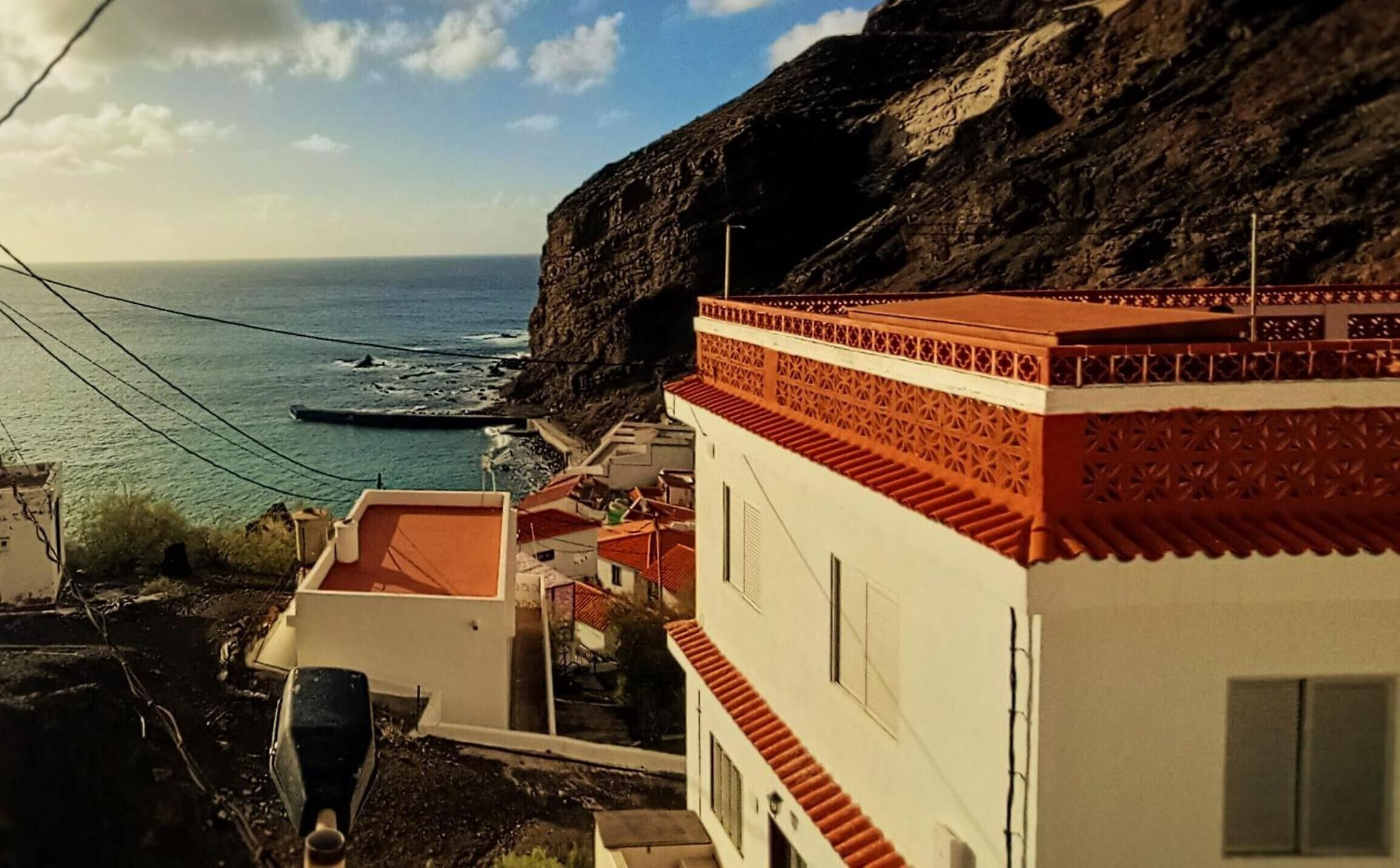 A coastal building with a red-tiled roof, a steep staircase, and a view of the sea.