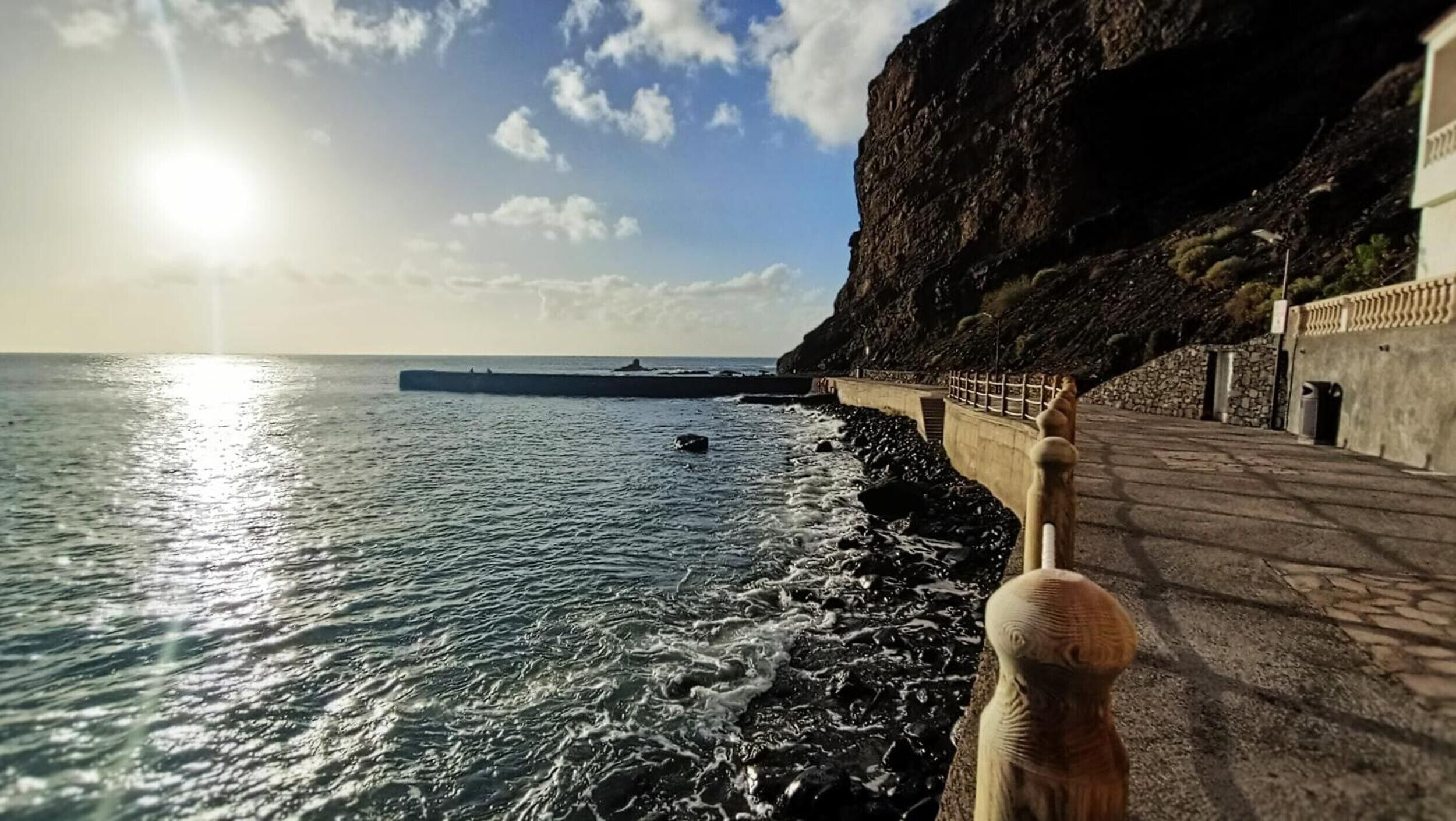 A coastal walkway with a rocky cliff, a clear sky, and the ocean.