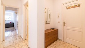 Een gang met een houten dressoir, een spiegel en een deur met decoratief paneel.