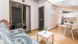 Een woonkamer met een bank, een bijzettafeltje met een vaas, en een schuifdeur naar een balkon.