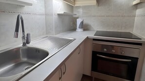 Een keuken met een roestvrijstalen spoelbak, een inbouwoven en lichtgekleurde kastjes.