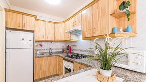 A kitchen with wooden cabinets, a refrigerator, a stove, a microwave, and a potted plant. - Vacation Apartment 'Alquilaencanarias-el Médano Delfines' with Balcony and Wi-Fi (El Médano)