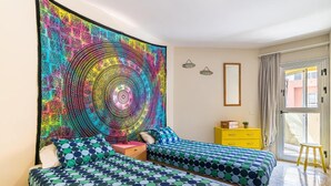 A room with two beds, a colorful tapestry, a yellow dresser, and a window with a view. - Vacation Apartment 'Alquilaencanarias-el Médano Delfines' with Balcony and Wi-Fi (El Médano)