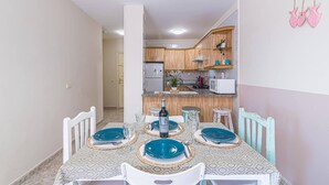 A dining area with a table set for four, a kitchen in the background, and a decorative wall hanging. - Vacation Apartment 'Alquilaencanarias-el Médano Delfines' with Balcony and Wi-Fi (El Médano)