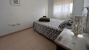 Une chambre à coucher comprenant un lit, une table de chevet, une fenêtre avec des rideaux, une prise de courant fixée au mur et un tableau encadré.