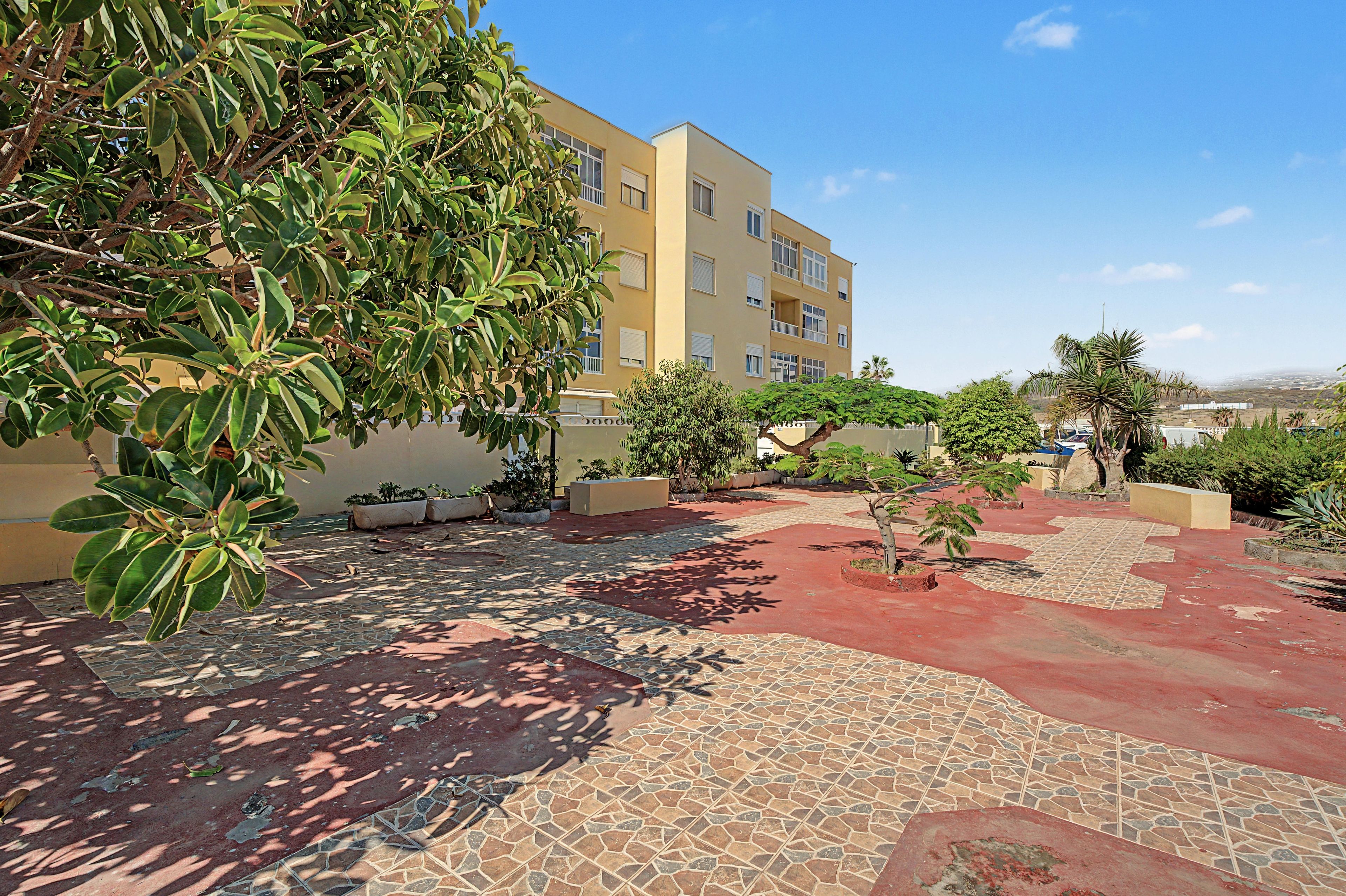 A courtyard with a tiled floor, surrounded by buildings and greenery.