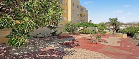 A courtyard with a tiled floor, surrounded by buildings and greenery.