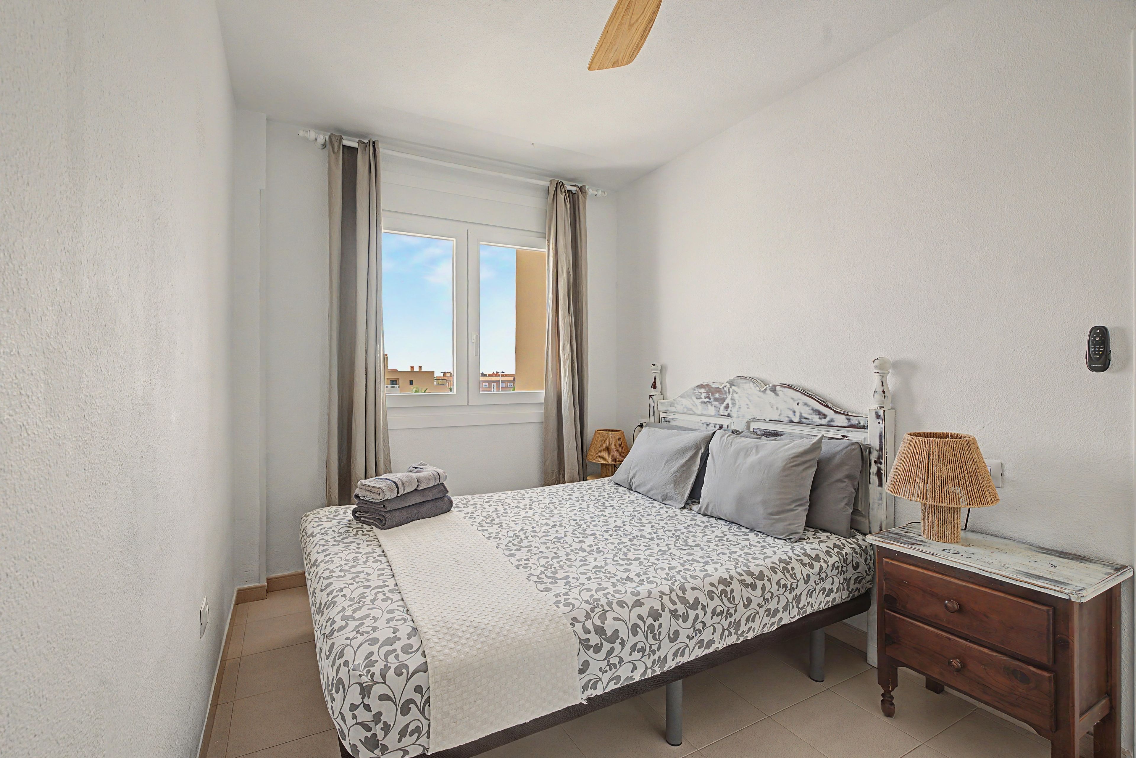 A bedroom with a bed, a nightstand, a lamp, and a window with curtains.
