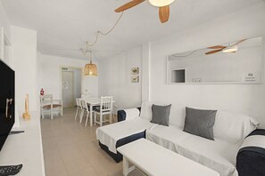 A hotel room with a white sofa, a small table, a ceiling fan, and a mirror on the wall. - Vacation Apartment 'Alquilaencanarias-medano Lagos De' with Mountain View, Pool & Wi-Fi (El Médano)