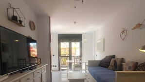 A modern living room with a flat-screen TV, a ceiling fan, a sofa, and a dining area with chairs. - Vacation Apartment 'Alquilaencanarias Duplex Beach' with Balcony and Wi-Fi (El Médano)