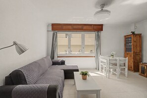 A living room with a sofa, a table, a cabinet, and a window with curtains. - Vacation Apartment 'Alquilaencanarias-medano Tío' with Wi-Fi (El Médano)