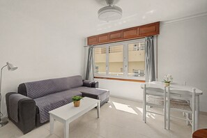 Una sala de estar moderna con un sofá gris, una mesa de centro blanca, una mesita pequeña blanca y una silla blanca.
