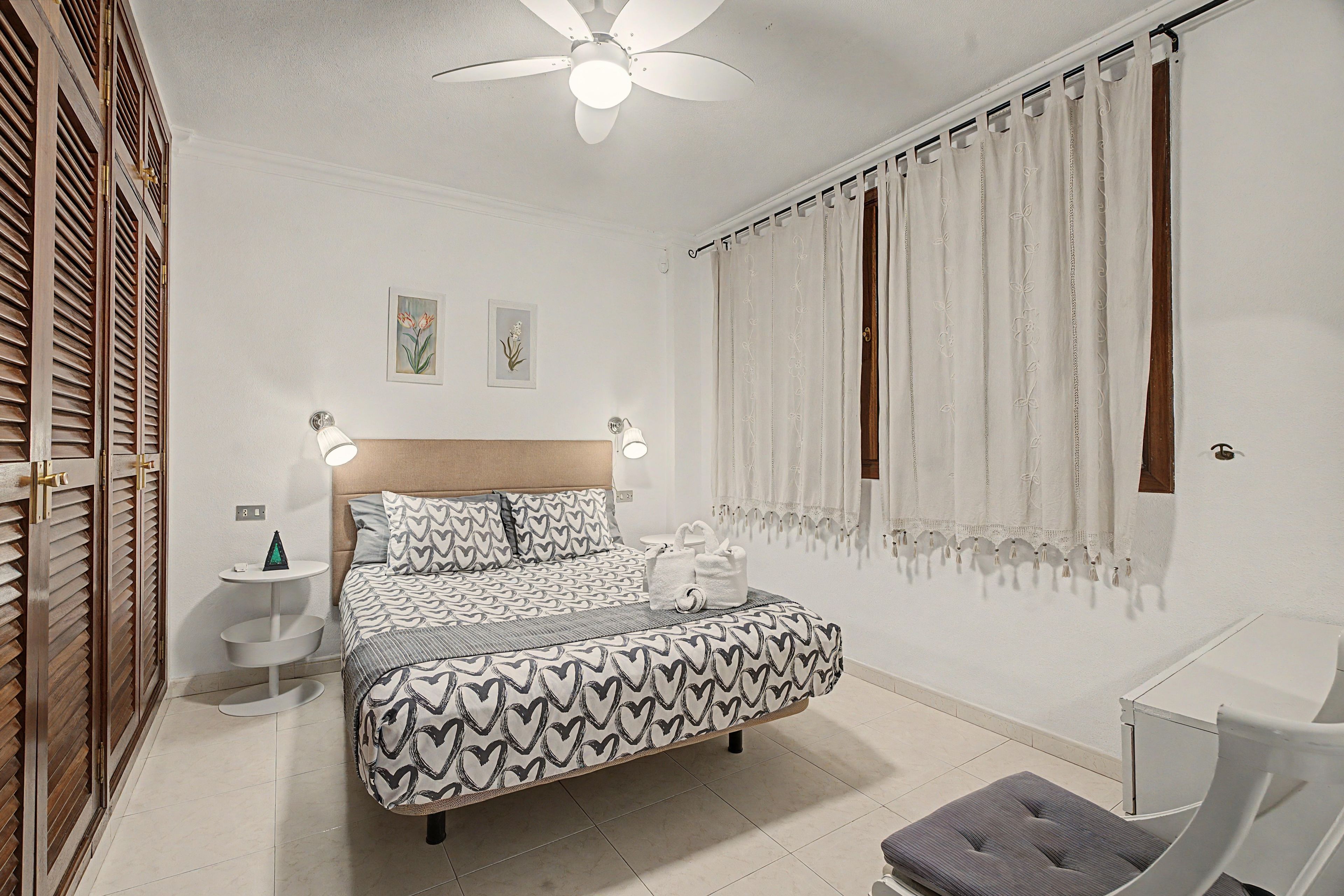 Ein Schlafzimmer mit einem Bett, Nachttischen, einem Deckenventilator und Vorhängen.