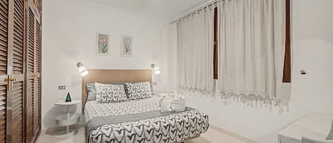 Une chambre à coucher avec un lit, des tables de chevet, un ventilateur de plafond et des rideaux.