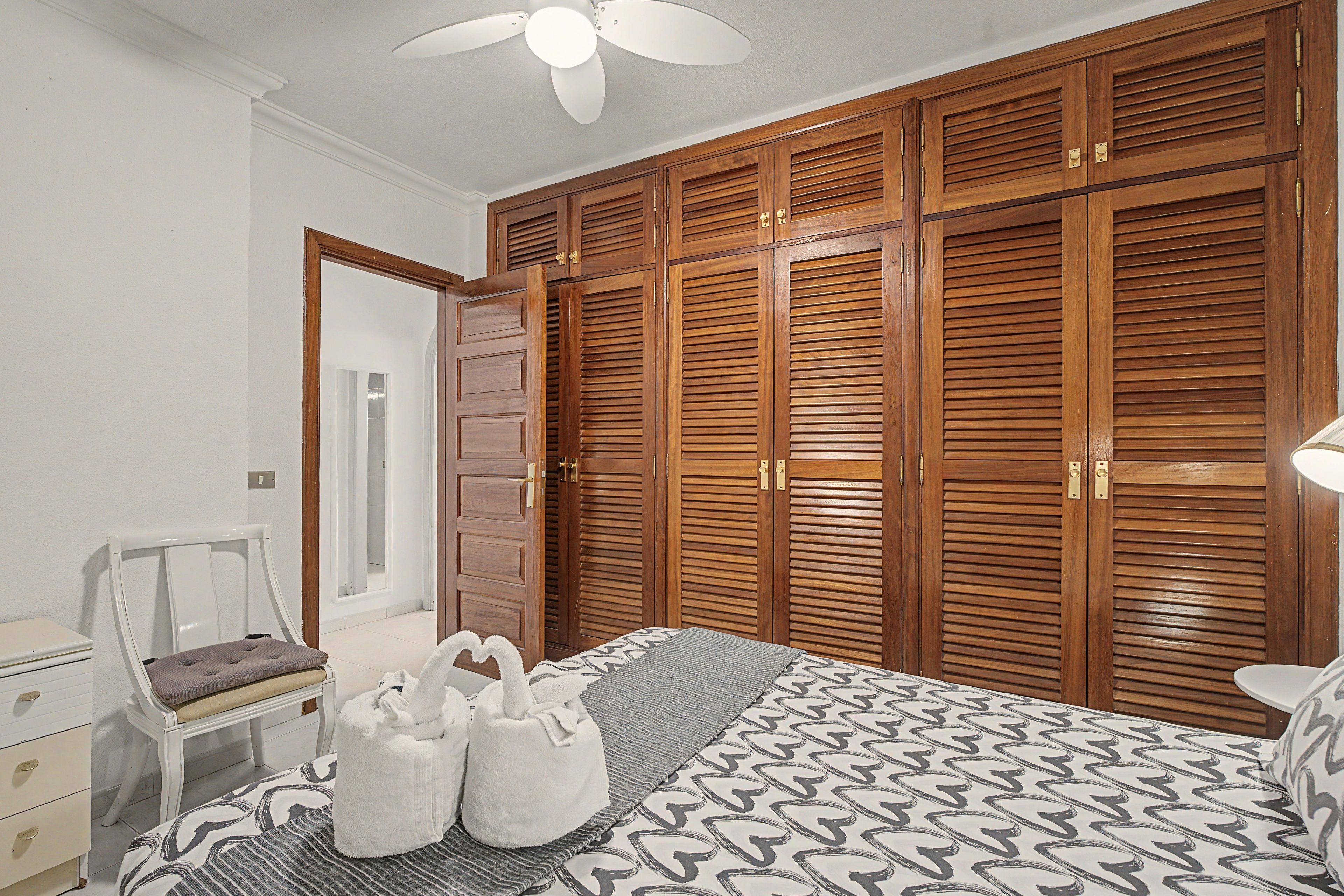 A bedroom with a bed, a chair, a wardrobe, and a ceiling fan.