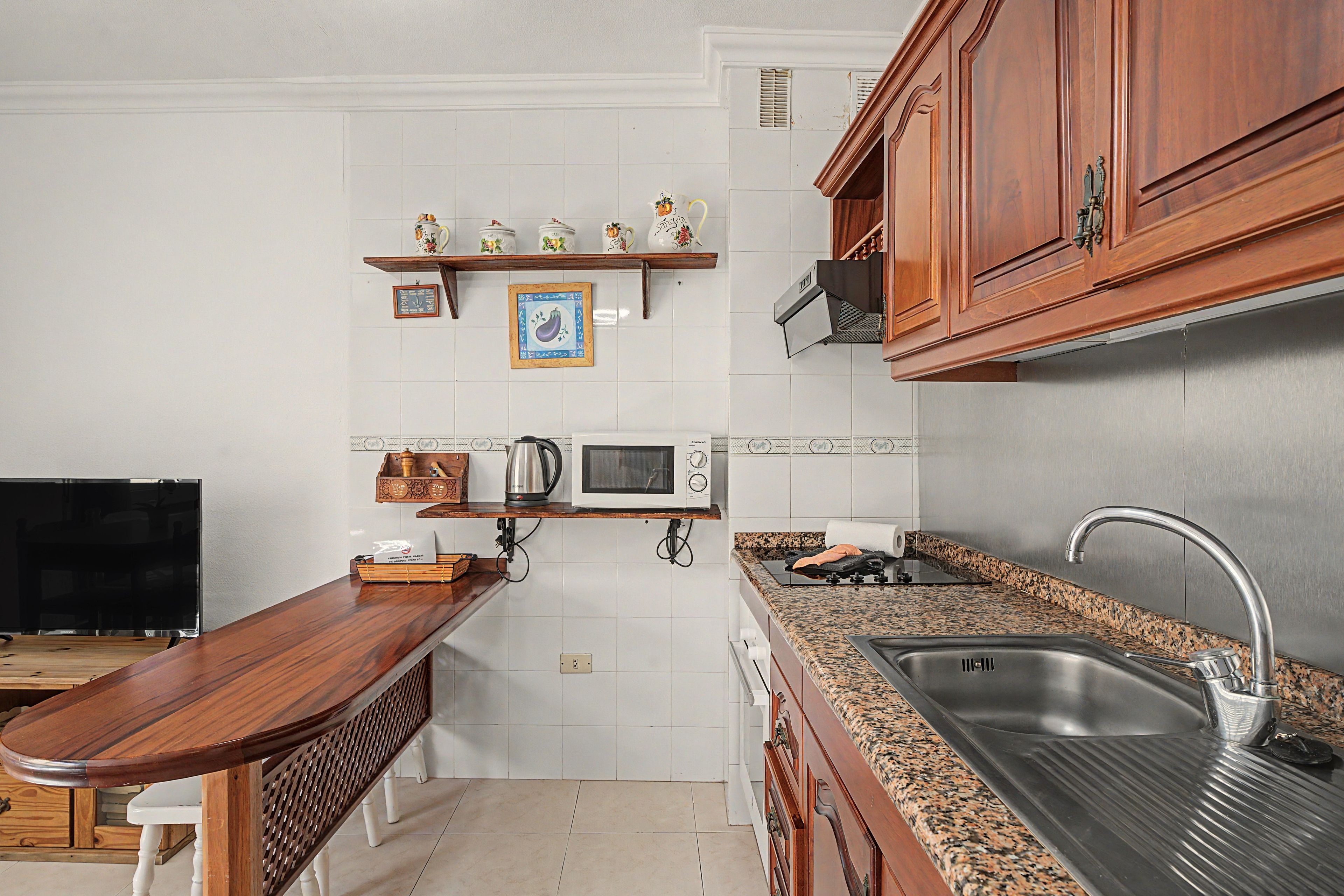 A kitchen with wooden cabinets, a stainless steel sink, a microwave, and a wooden countertop.