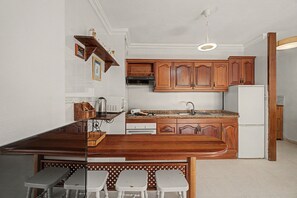 A kitchen with wooden cabinets, a white refrigerator, a countertop with a sink, and a dining area with stools. - Vacation Apartment 'Alquilaencanarias-medano Tío' with Wi-Fi (El Médano)