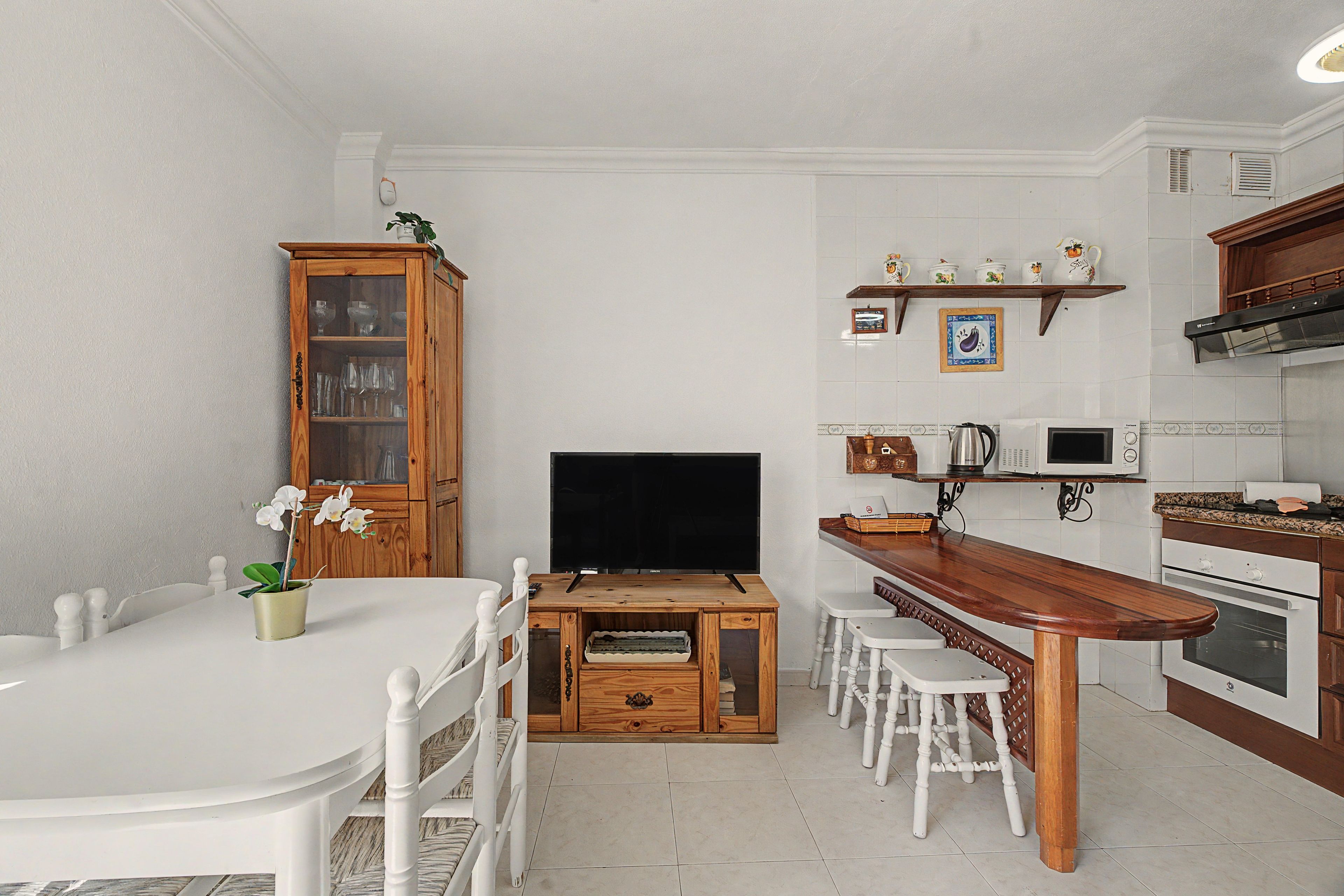 Un angolo cottura compatto con mobili bianchi, un tavolo da pranzo in legno e un televisore.