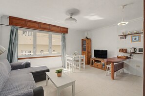 Un espacio habitable compacto con sofá, mesa de comedor, zona de cocina y televisor.