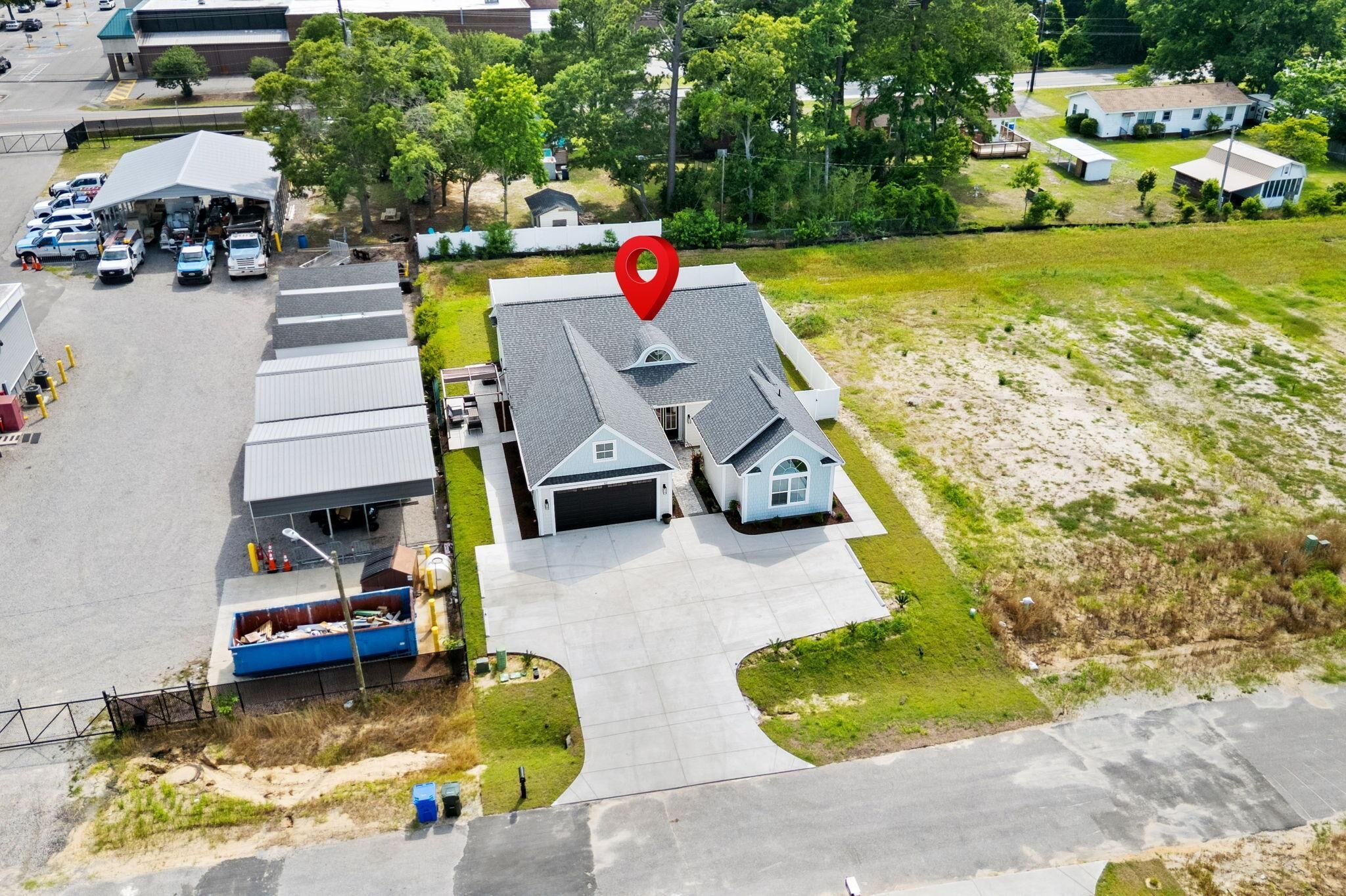 An aerial view of a residential area with a house, a covered area with parked cars, and a red location marker.