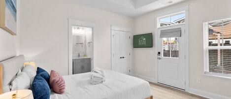 A bedroom with a bed, a ceiling fan, a bathroom with a mirror, a door, and a window with blinds.