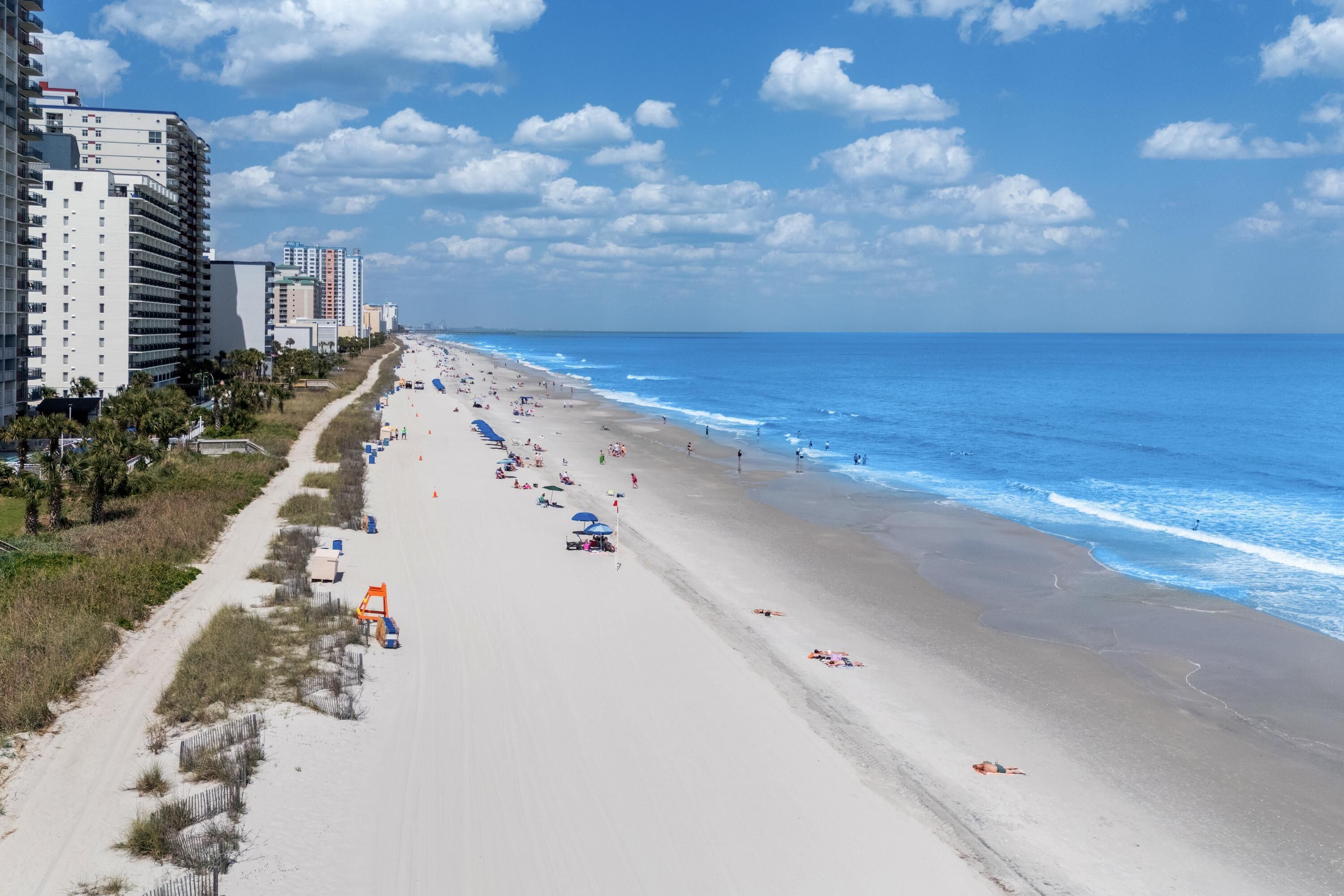 A beach with buildings, a clear sky, and a sandy shore.