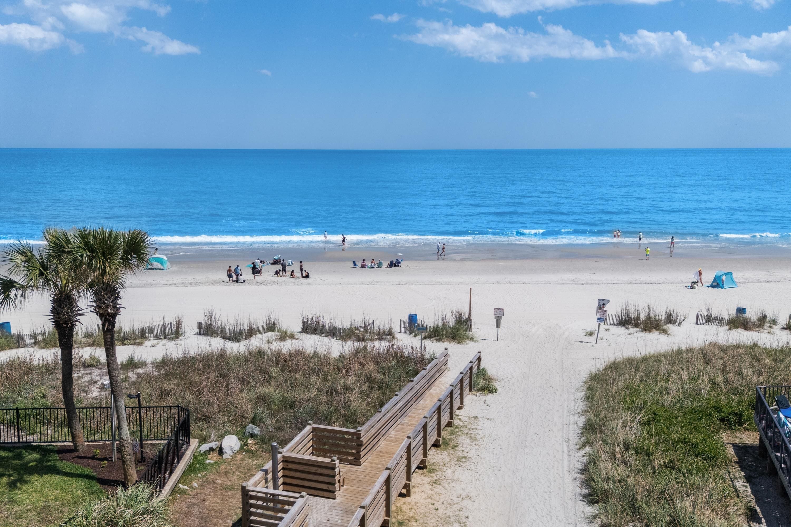 A beach with a wooden boardwalk, a tent, and a clear view of the ocean.