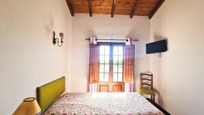 A room with a bed, a chair, a television, and a window with curtains.