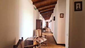 A hallway with wooden beams, numbered rooms, and striped chairs.
