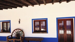 A rustic building with a wooden porch, a large wooden wheel, and a bench.