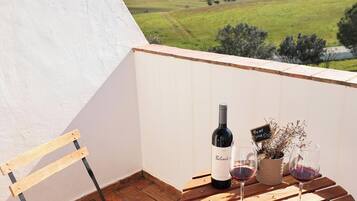 A balcony with a wine bottle and glasses, a wooden chair, and a view of a green landscape.