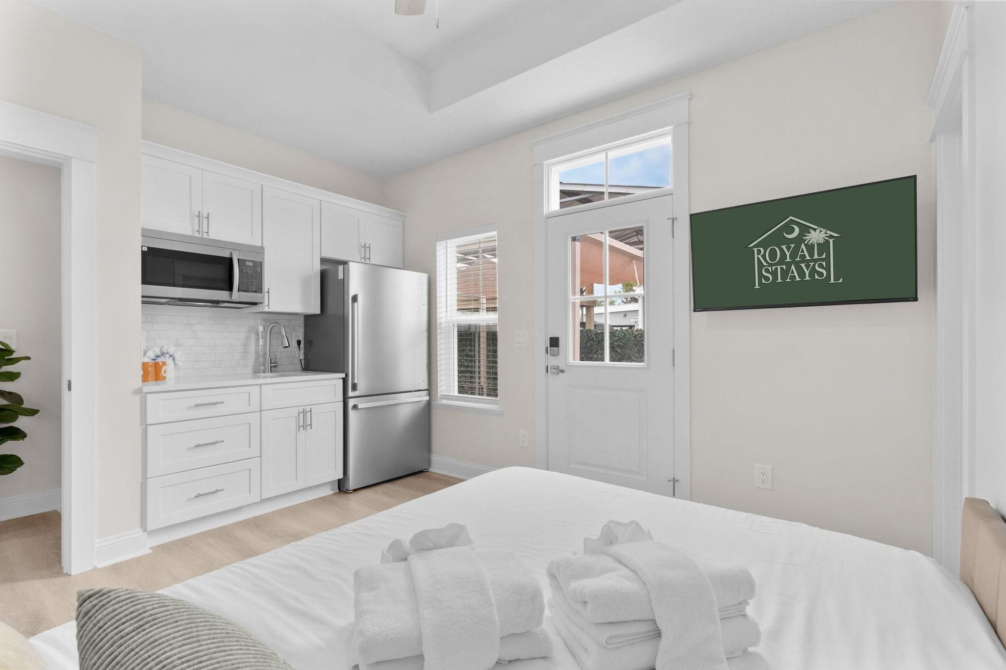 A modern hotel room with a kitchenette, a bed with white linens, and a view of the outside.