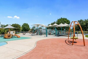 Un parque infantil con diversas estructuras de juego, como toboganes y columpios, bajo zonas sombreadas.